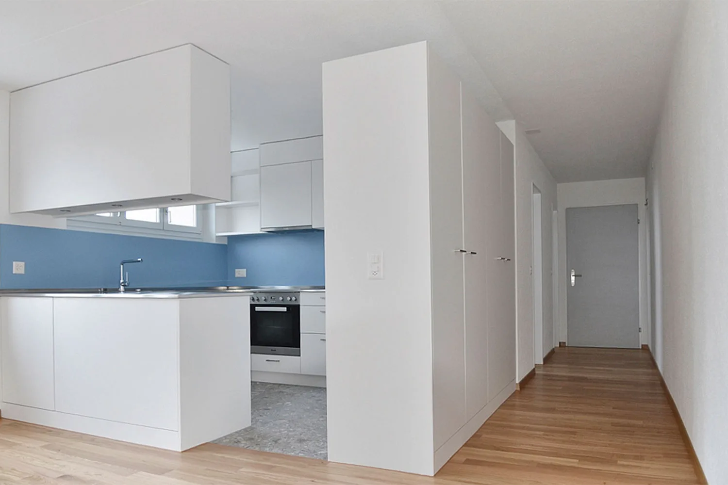 MFH Kirchfeldstrasse – Sanierte Wohnung: neue Küche mit blauem Spritzschutz und Korridor
